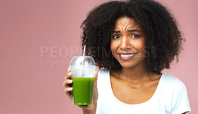 Buy stock photo Studio shot of an attractive young woman drinking green juice and looking nervous against a pink background