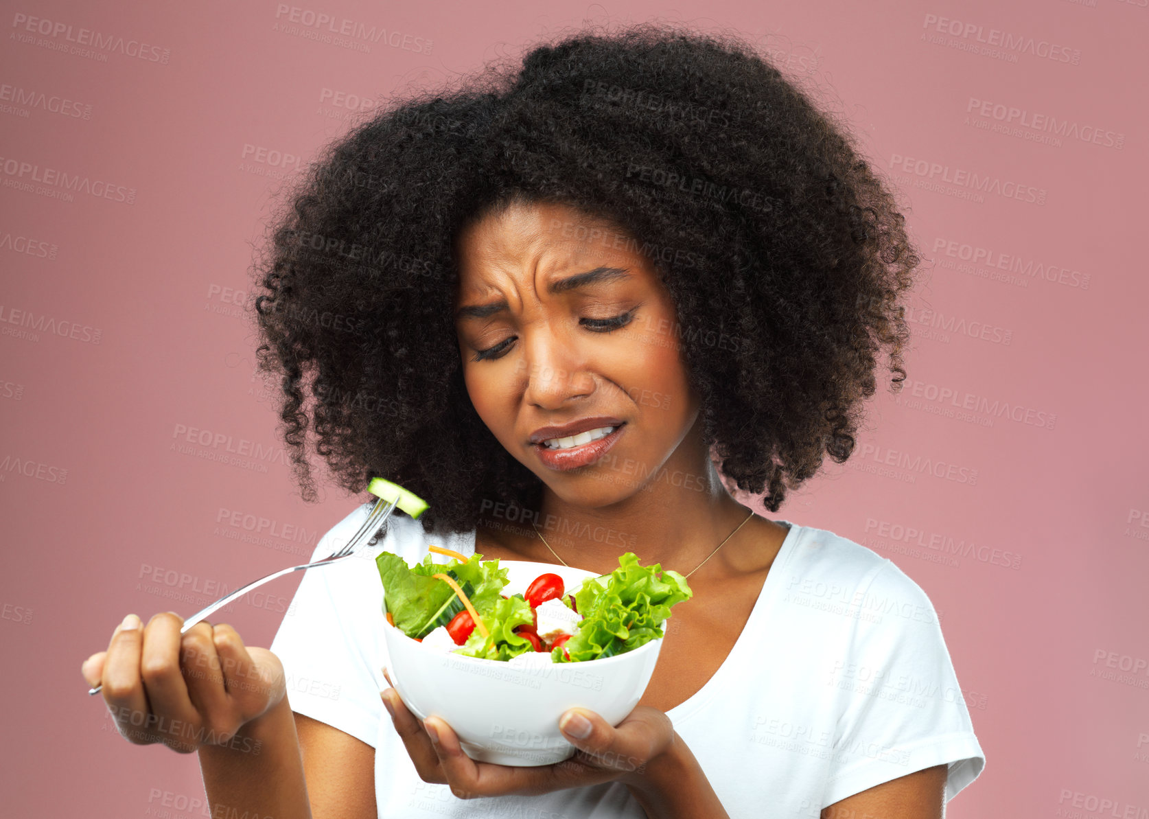 Buy stock photo Unhappy, salad and dislike of black woman in studio eating vegetables for nutrition or vegan diet. Girl, pink background and health for food, detox and wellness benefits for weight loss and disgust