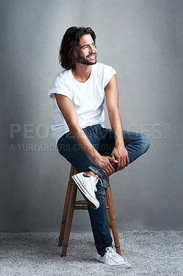 Buy stock photo Studio shot of a handsome young man sitting on a stool against a grey background