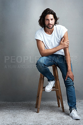 Buy stock photo Studio shot of a handsome young man sitting on a stool against a grey background