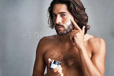Buy stock photo Studio shot of a handsome young man applying moisturiser to his face against a grey background