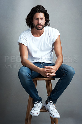 Buy stock photo Fashion, handsome and portrait of man in studio on a stool with casual, cool and stylish outfit. Confidence, serious and young male model from Mexico with trendy style on chair by gray background.
