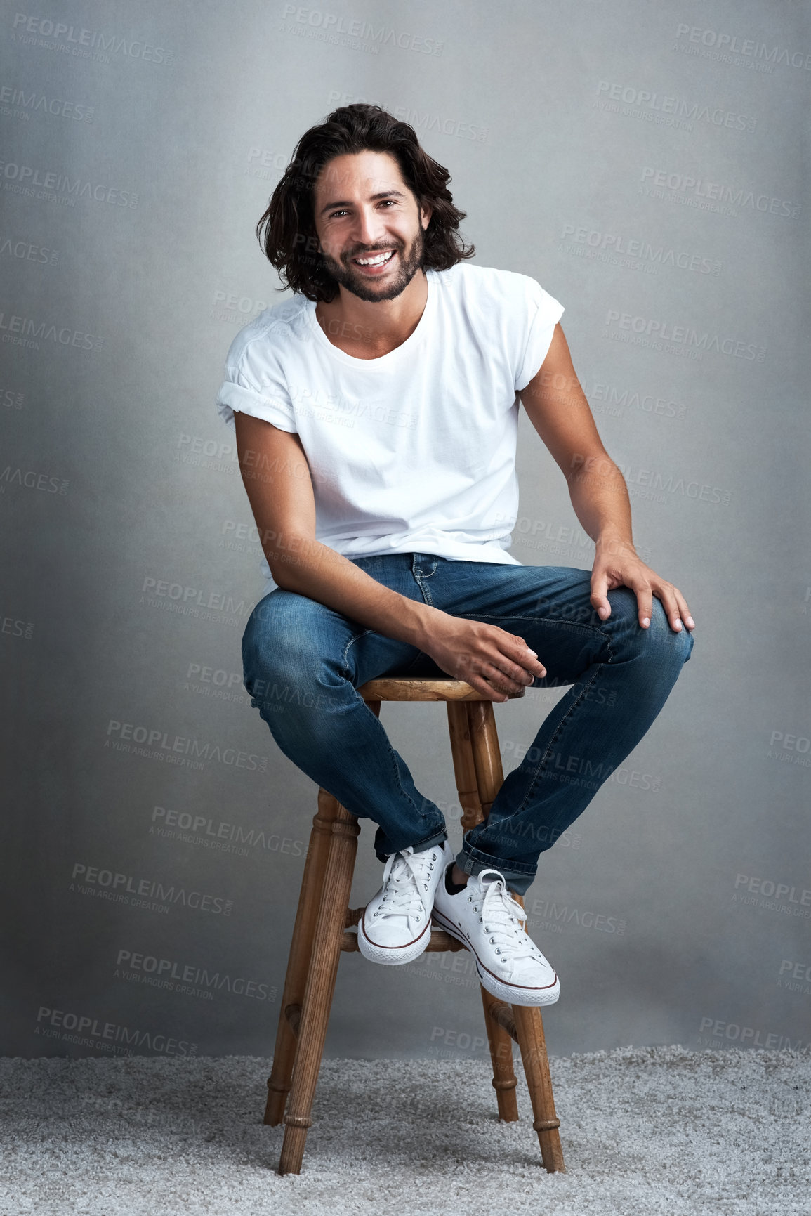 Buy stock photo Fashion, happy and portrait of man in studio on a stool with casual, cool and stylish outfit. Smile, handsome and confident young male model from Mexico with trendy style on chair by gray background.