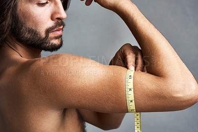 Buy stock photo Studio shot of a handsome young man measuring his bicep against a grey background