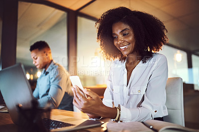 Buy stock photo Shot of a young businesswoman using a cellphone while working alongside her colleague in an office at night
