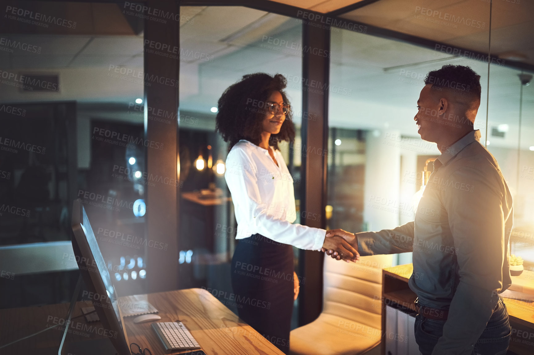 Buy stock photo Shot of two businesspeople shaking hands in an office at night