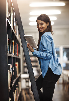 Buy stock photo Shot of a university student using a ladder to reach a book in the library at campus