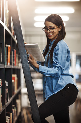 Buy stock photo Shot of a university student using a ladder to reach a book in the library at campus