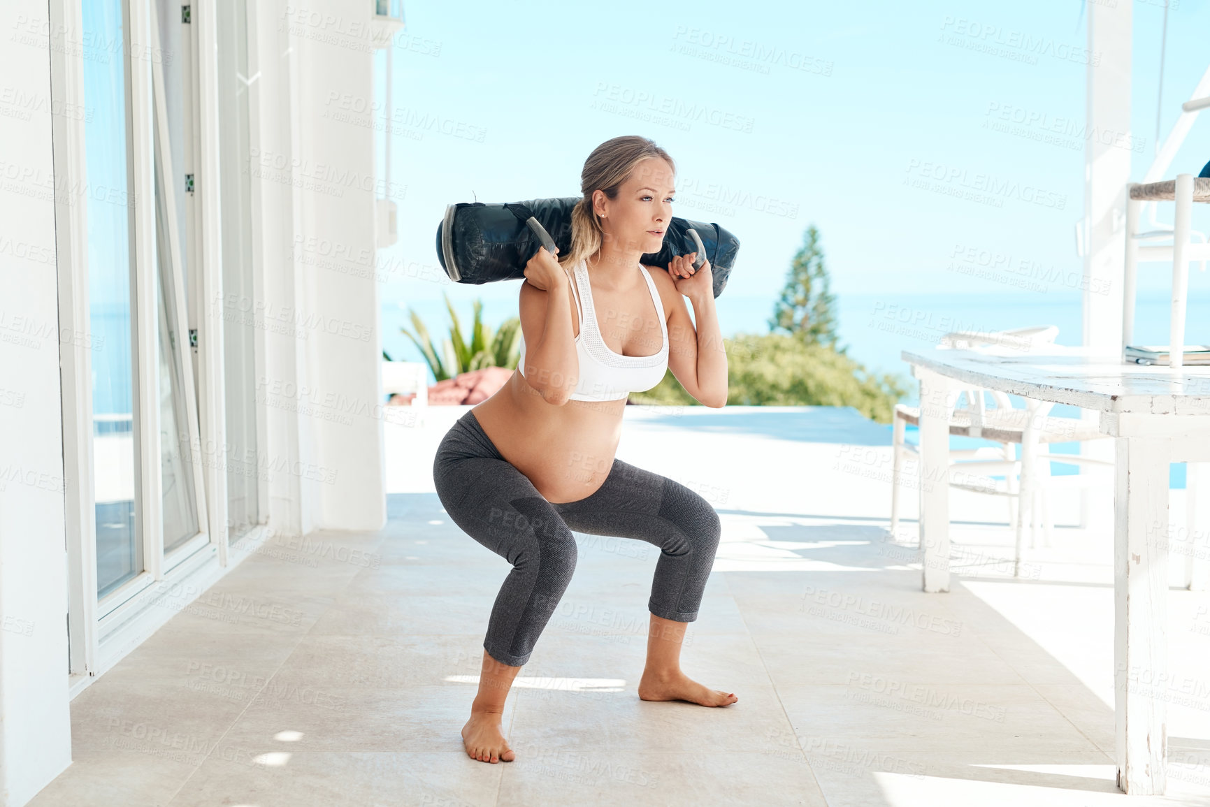 Buy stock photo Shot of a pregnant woman working out with a sand bag on the patio at home
