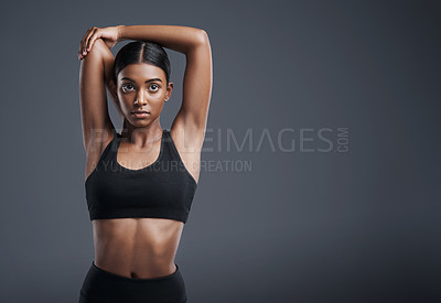 Buy stock photo Studio portrait of a sporty young woman stretching her arms against a grey background
