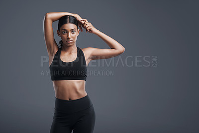 Buy stock photo Studio portrait of a sporty young woman stretching her arms against a grey background