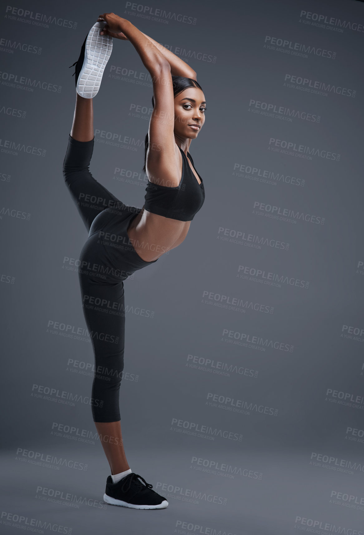 Buy stock photo Studio portrait of a sporty young woman stretching her body against a grey background