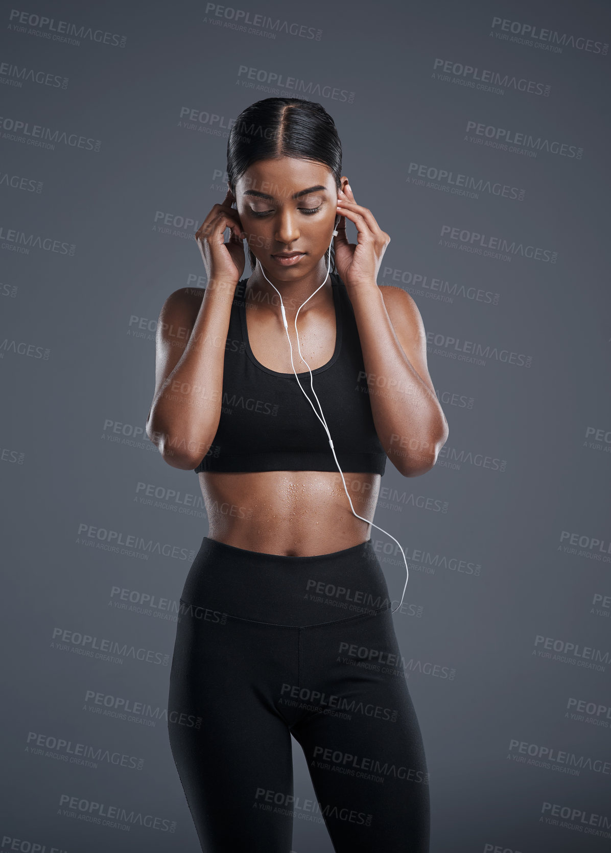 Buy stock photo Indian woman, fitness and earphones in studio for music, listening and podcast by dark background. Female athlete, streaming and audio for workout, sports and thinking of playlist for training