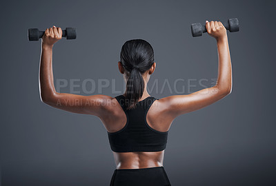 Buy stock photo Studio shot of a sporty young woman lifting weights against a grey background