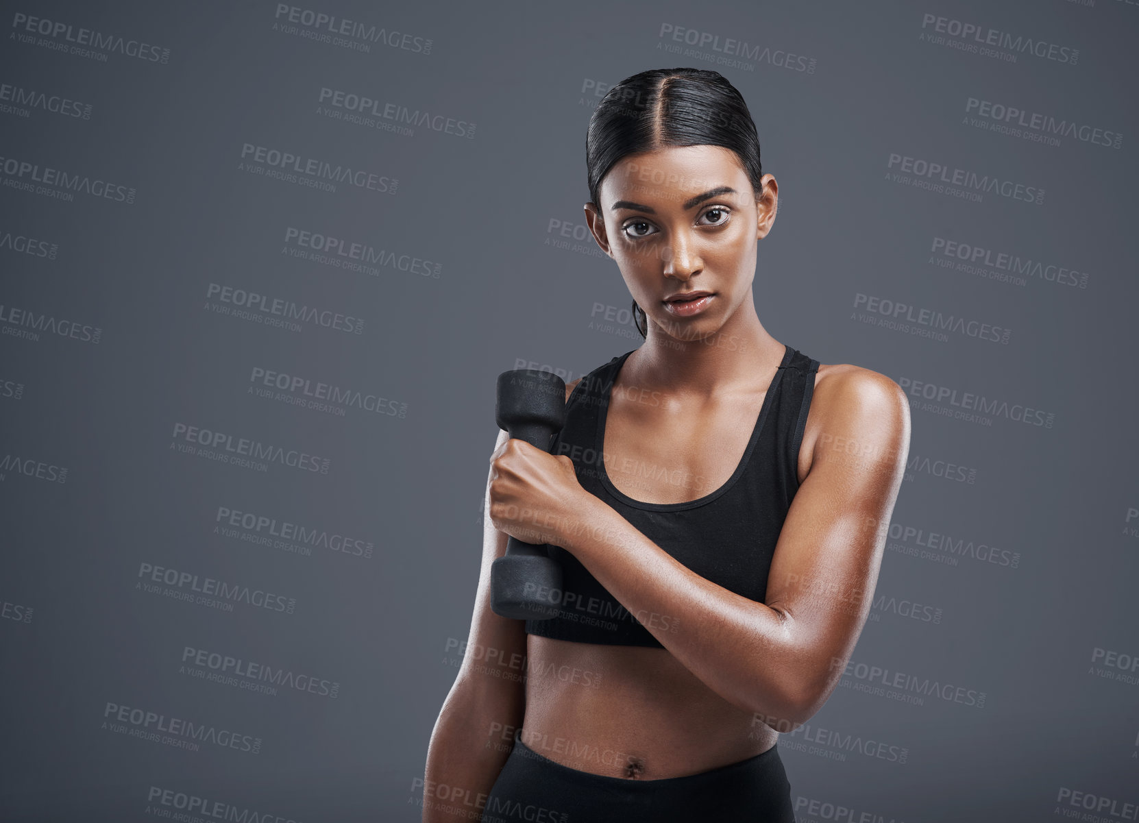 Buy stock photo Studio portrait of a sporty young woman lifting weights against a grey background