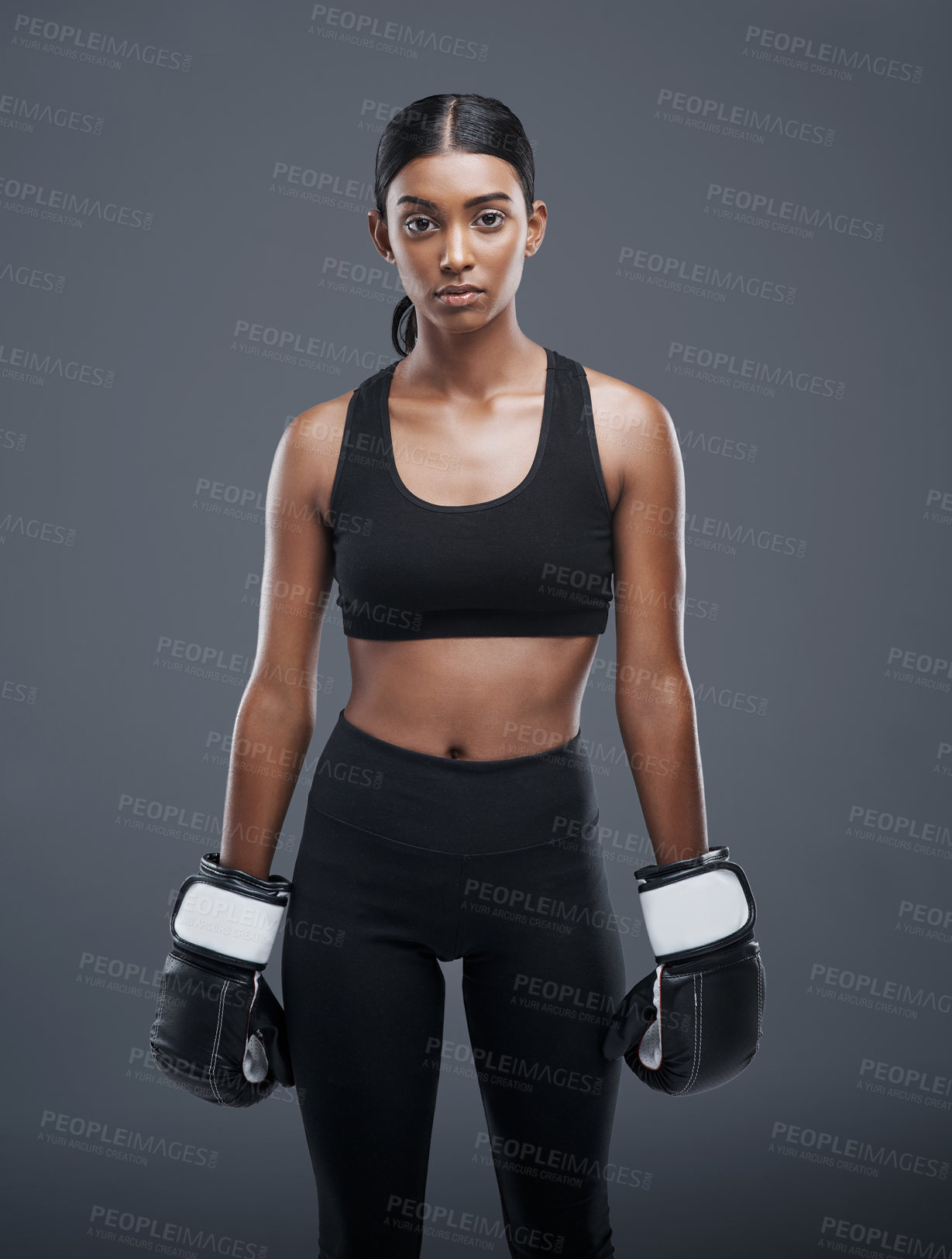 Buy stock photo Studio portrait of a sporty young woman wearing boxing gloves against a grey background