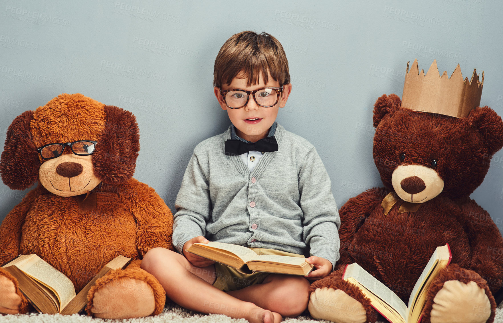Buy stock photo Studio portrait of a smart little boy reading a book next to his teddy bears against a gray background