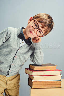 Buy stock photo Studio portrait of a smart little boy leaning over a pile of books against a gray background