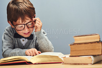 Buy stock photo Studio shot of a smart little boy reading books against a gray background