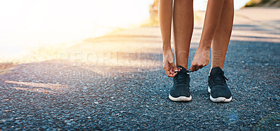 Buy stock photo Cropped shot of an unrecognizable young woman tying her shoelaces while exercising outdoors