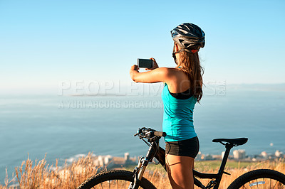 Buy stock photo Cropped shot of a young woman taking a picture of the beautiful scenery while out mountain biking