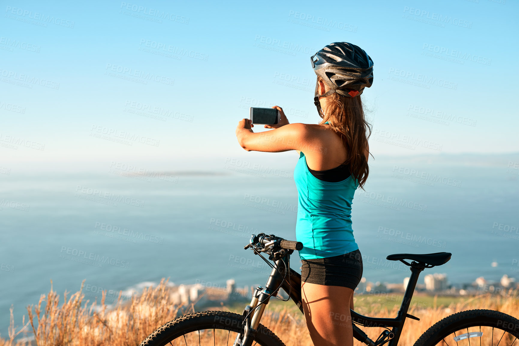 Buy stock photo Cropped shot of a young woman taking a picture of the beautiful scenery while out mountain biking