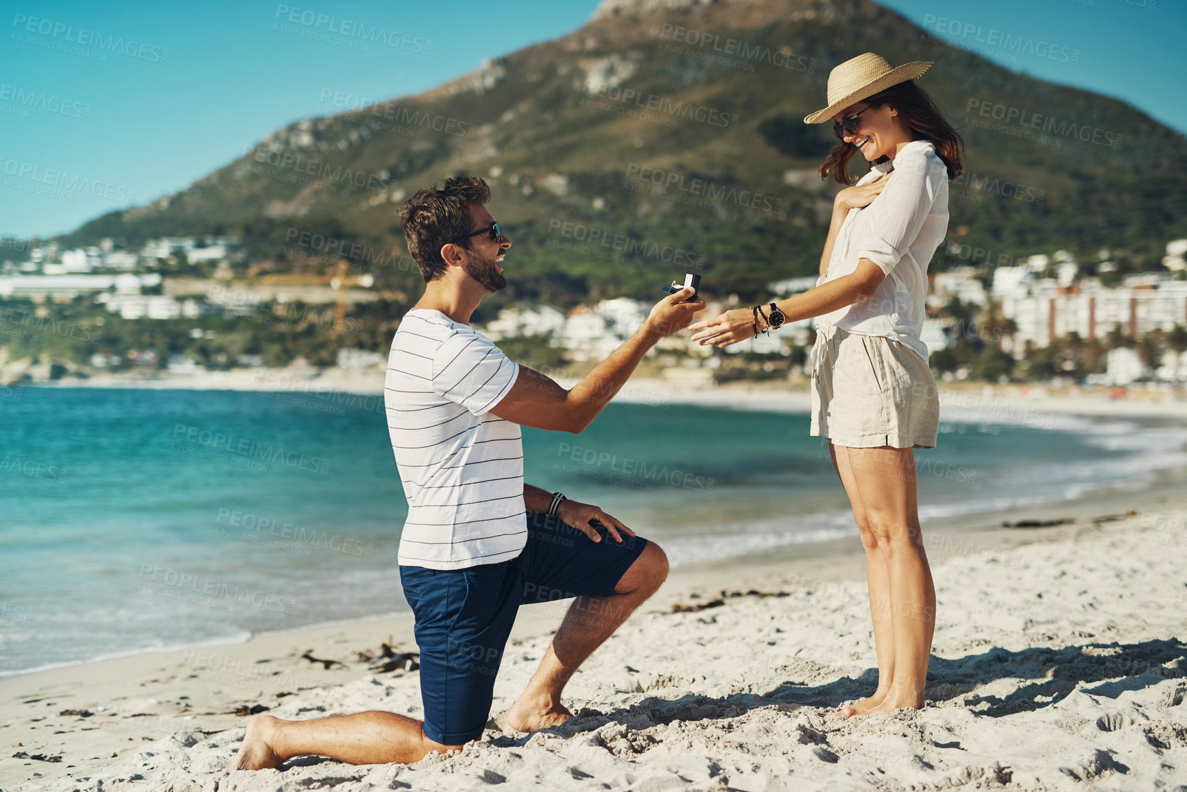 Buy stock photo Full length shot of a young man proposing to his girlfriend at the beach on a summer’s day