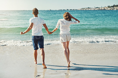 Buy stock photo Rearview shot of an unrecognizable and carefree young couple running along the beach
