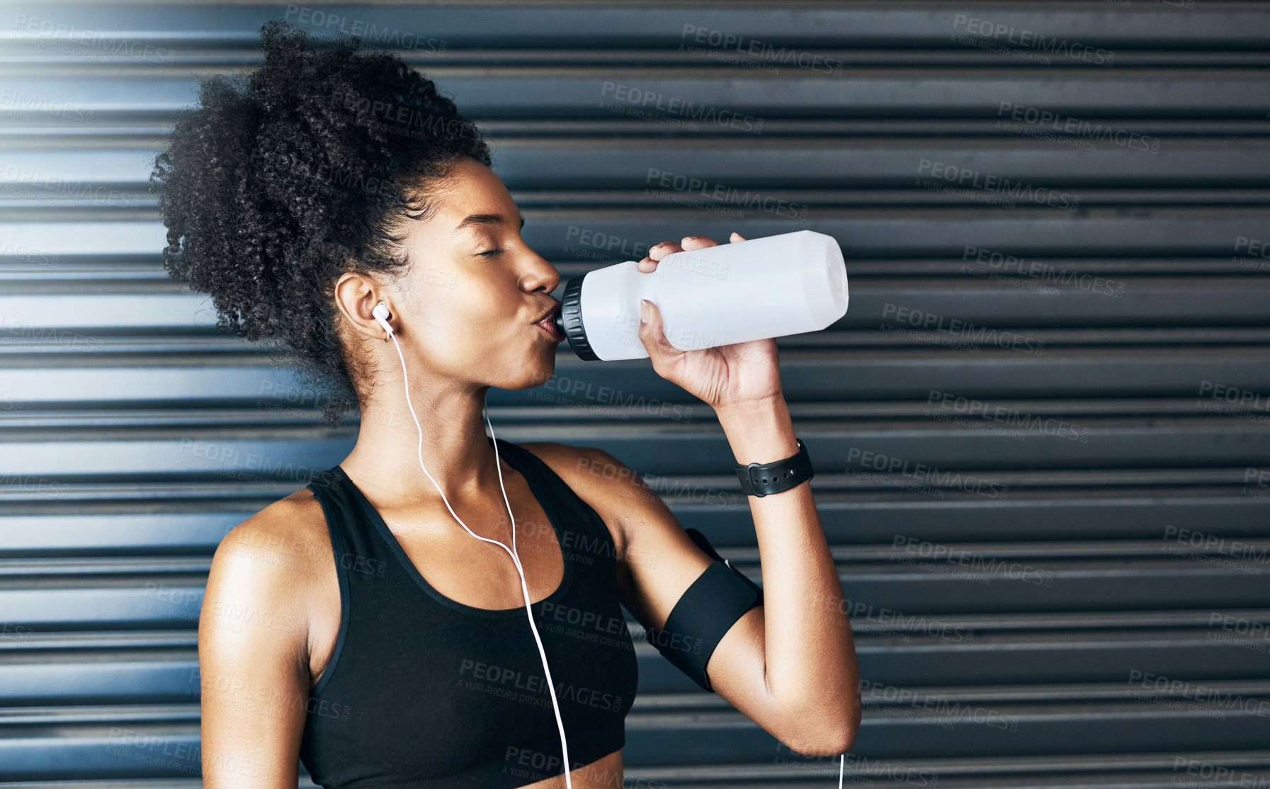 Buy stock photo Shot of a sporty young woman drinking water while exercising against a grey background