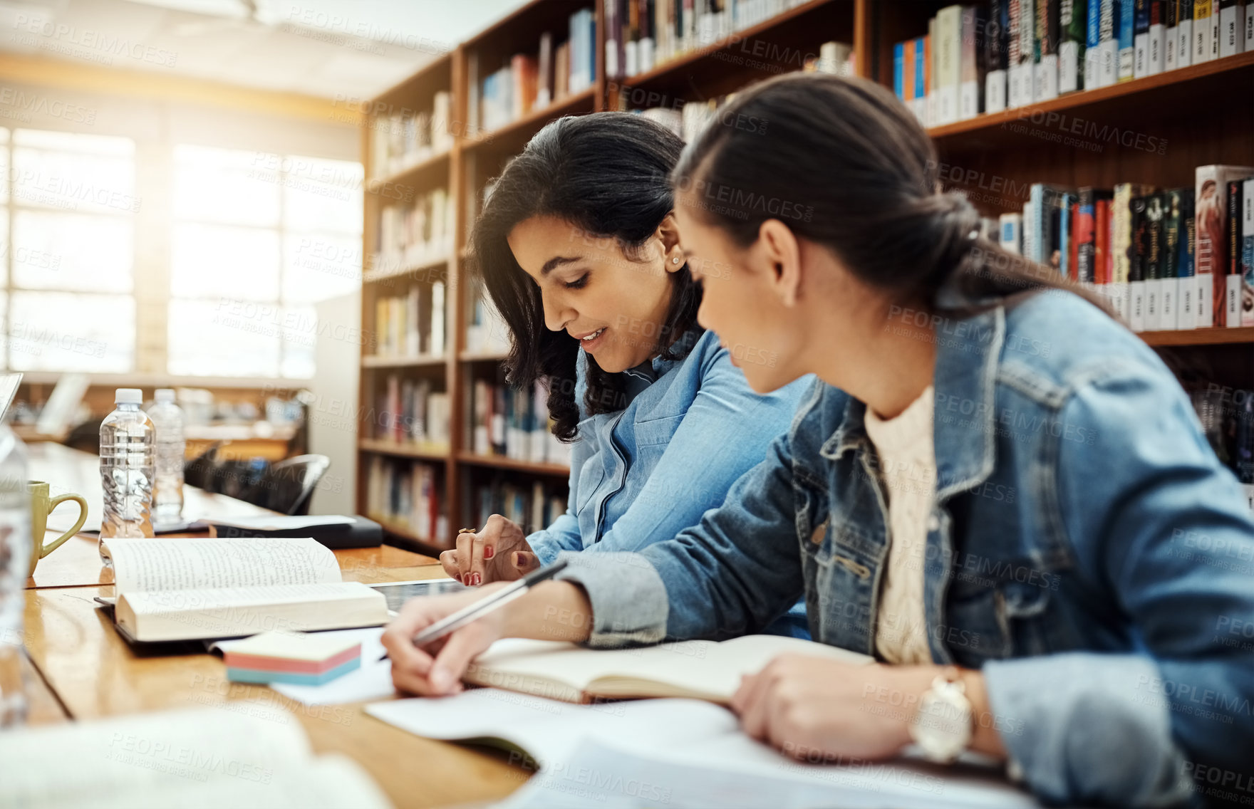Buy stock photo Cropped shot of two young female university students studying in the library