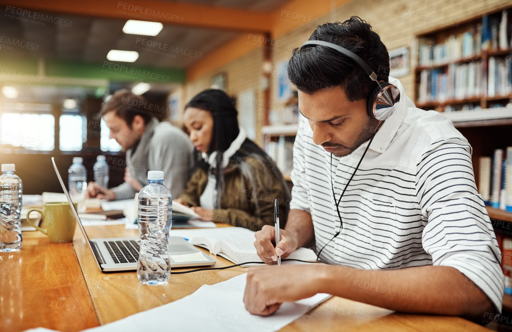 Buy stock photo Man, writing and notes in library for education, studying and headphones for music. Student, study group and research at laptop for knowledge, learning and exam preparation on university campus 