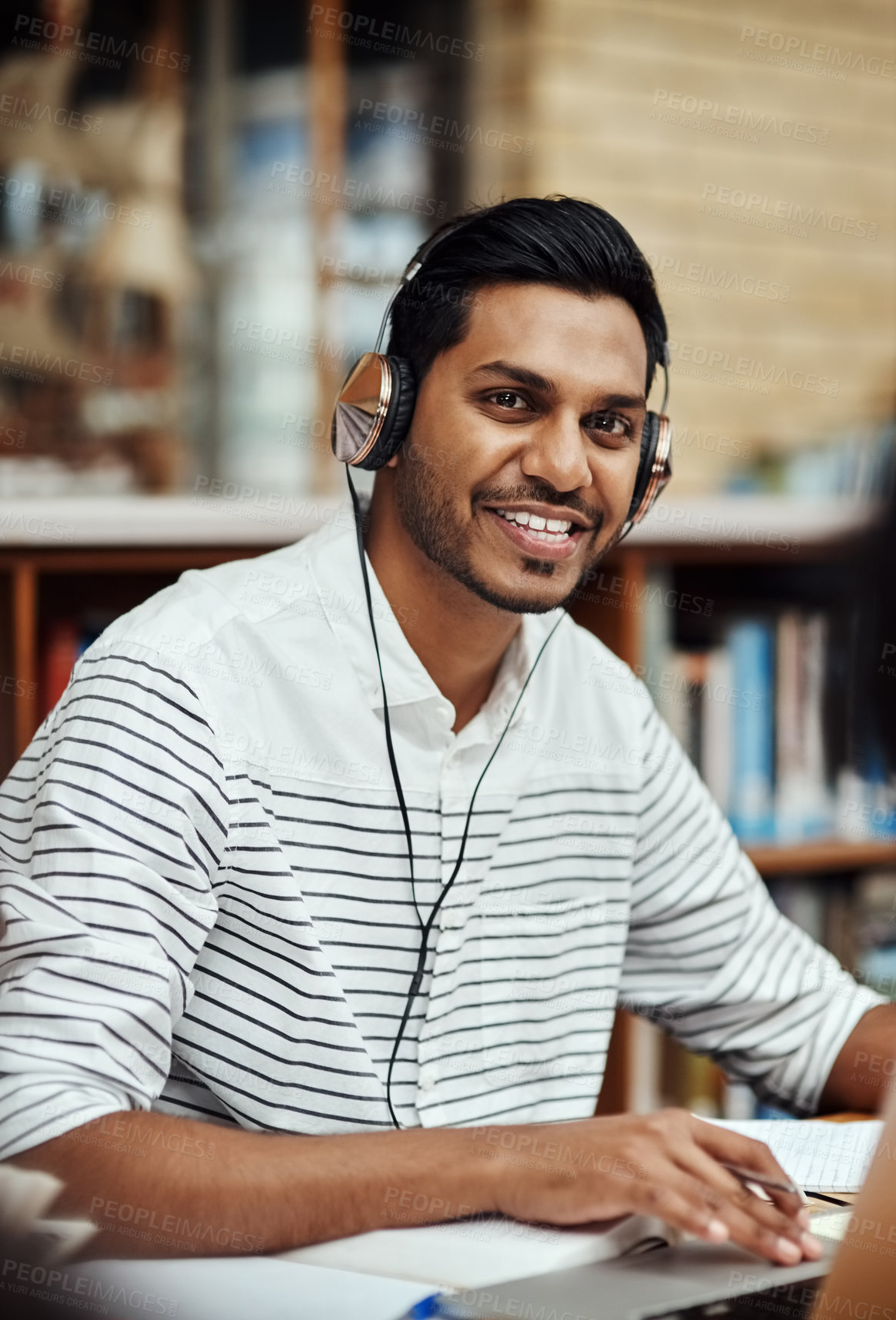 Buy stock photo Student, portrait and notes in library for education, studying and headphones for music. Man, smile and research at computer for knowledge, learning and exam preparation on university campus in India