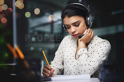 Buy stock photo Cropped shot of an attractive young businesswoman taking notes while working late in a call center