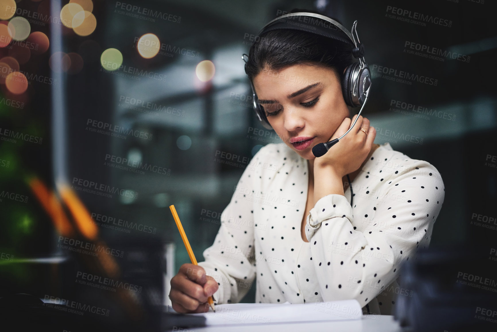 Buy stock photo Cropped shot of an attractive young businesswoman taking notes while working late in a call center