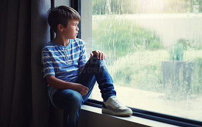 Buy stock photo Little boy, home and watching the rain by window of natural water drops and thinking in relax indoors. Child relaxing by windowsill looking out glass at storm in lonely or sad for weather at house