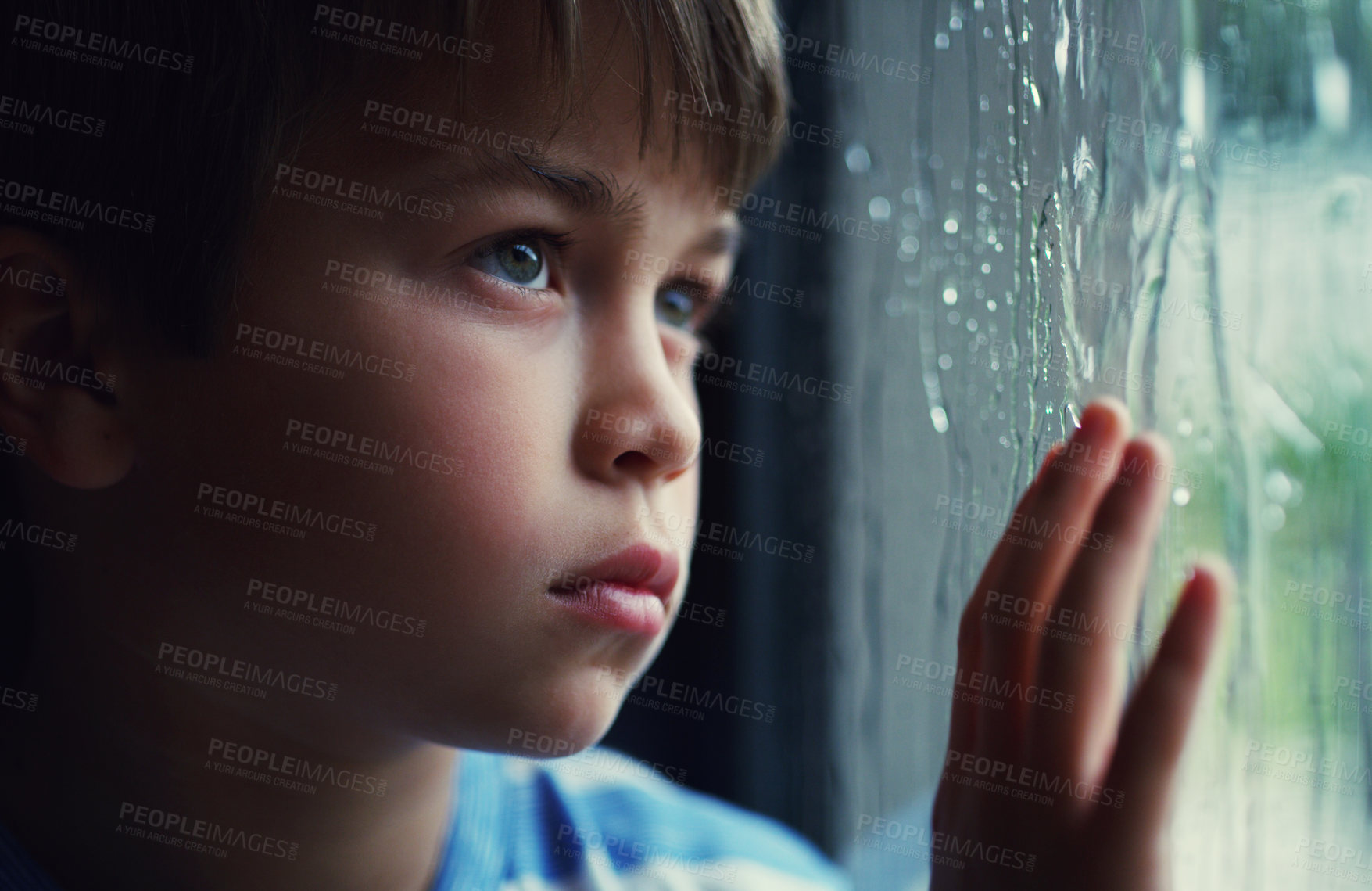 Buy stock photo Shot of a sad young boy watching the rain through a window at home