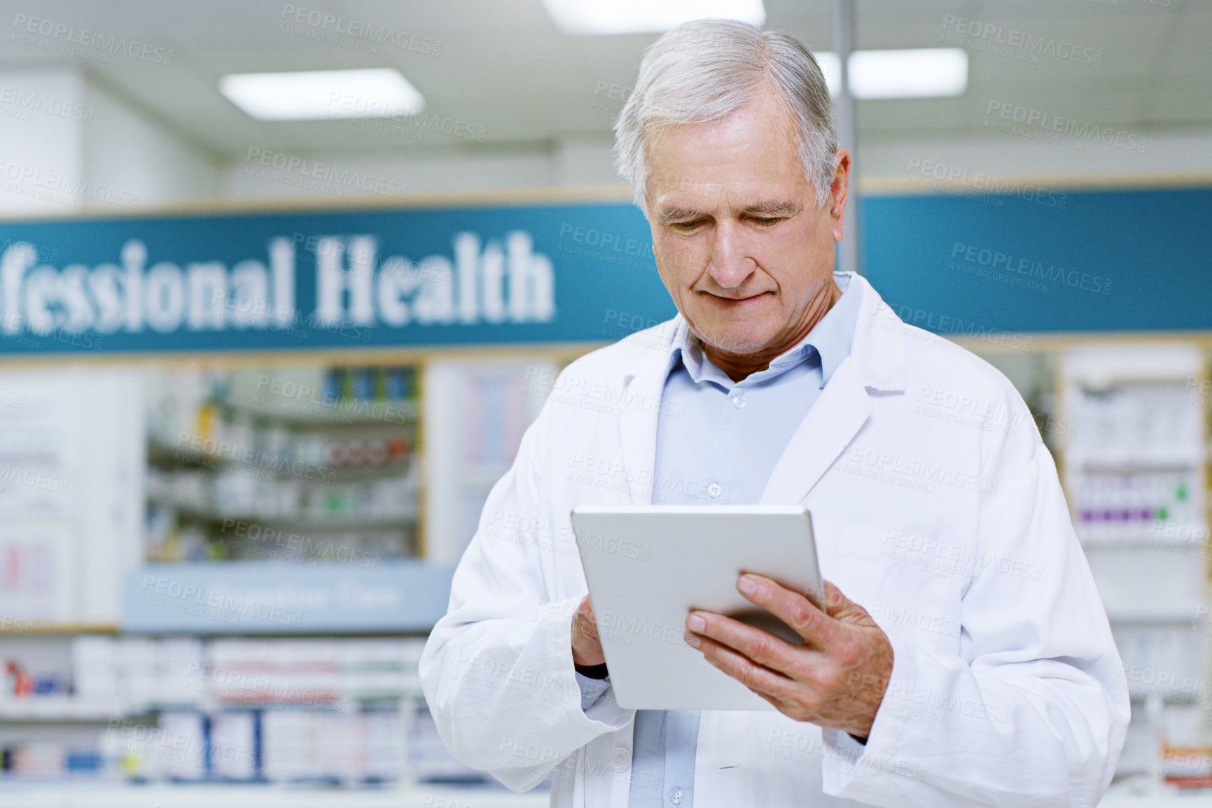 Buy stock photo Shot of a senior male pharmacist doing some work on his digital tablet