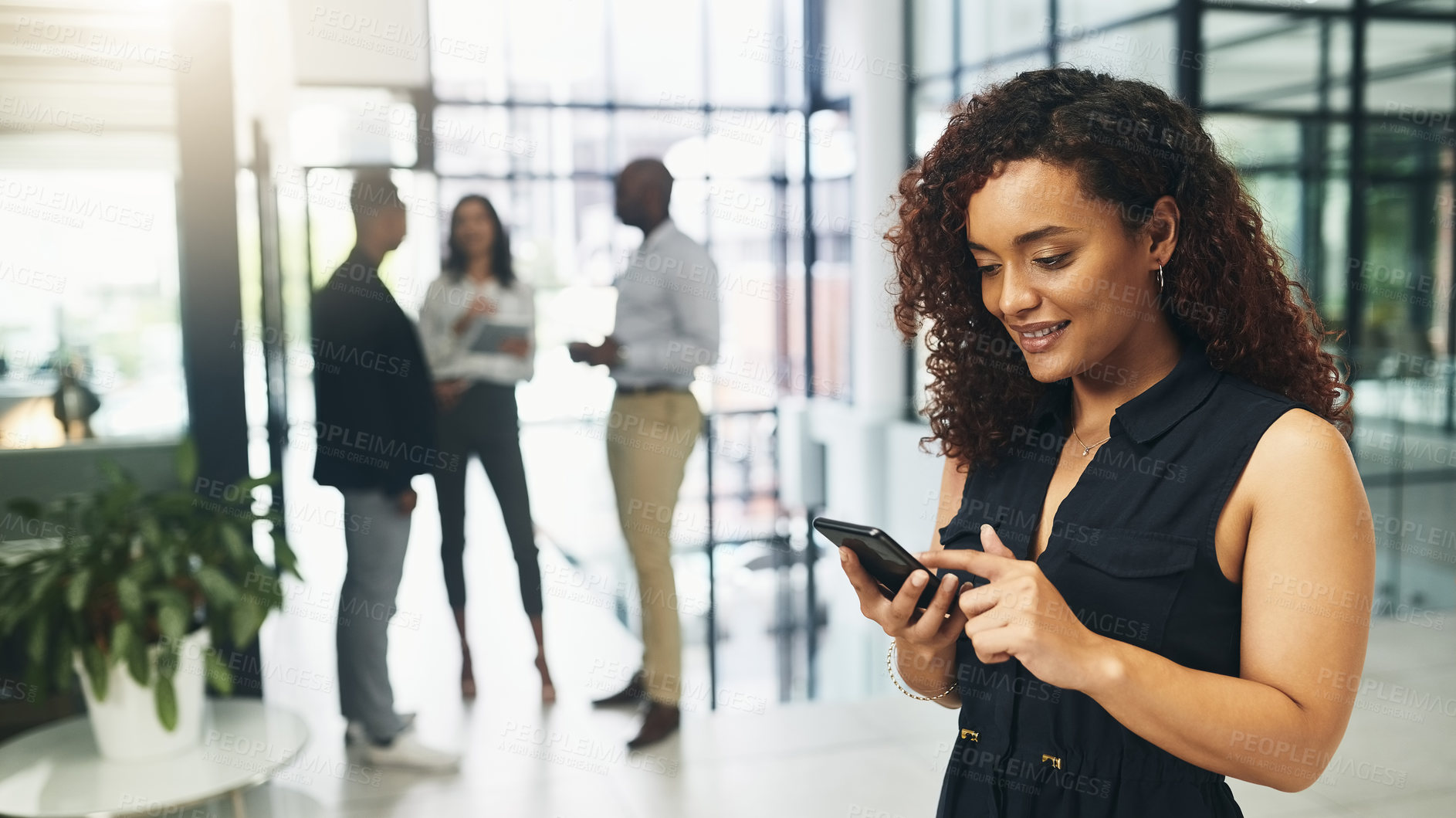 Buy stock photo Shot of a young businesswoman using a cellphone in an office with her colleagues in the background