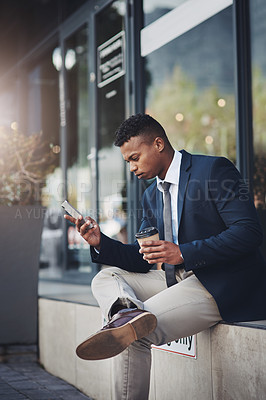 Buy stock photo Shot of a handsome young businessman using a cellphone while drinking coffee in the city