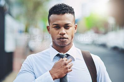 Buy stock photo Portrait of a handsome young businessman adjusting his tie while out in the city