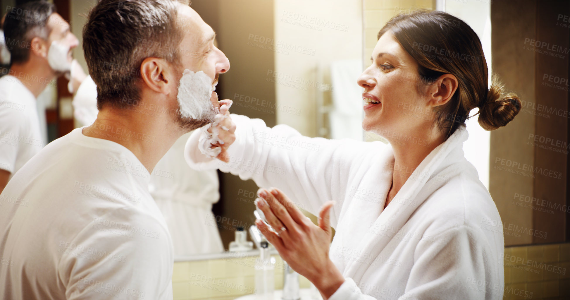 Buy stock photo Shot of a woman applying shaving cream to her husband's face in the bathroom at home