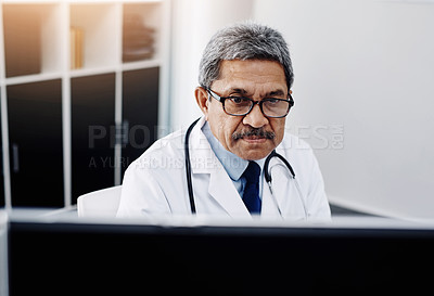 Buy stock photo Cropped shot of a focused mature male doctor working on a computer while being seated in his office during the day