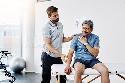 Buy stock photo Cropped shot of a young male physiotherapist helping a mature male patient with movement exercises at a clinic