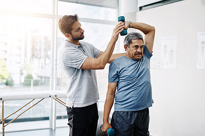 Buy stock photo Cropped shot of a young male physiotherapist helping a mature male patient with movement exercises at a clinic