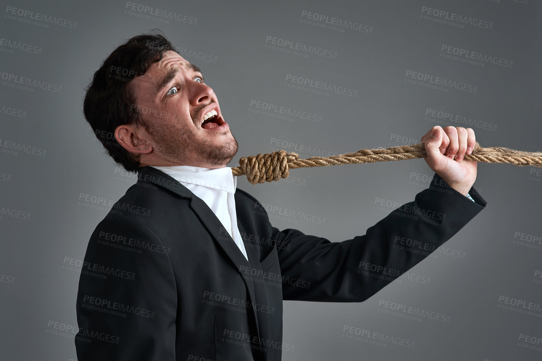 Buy stock photo Studio shot of a young businessman being pulled by a hangman’s noose against a gray background