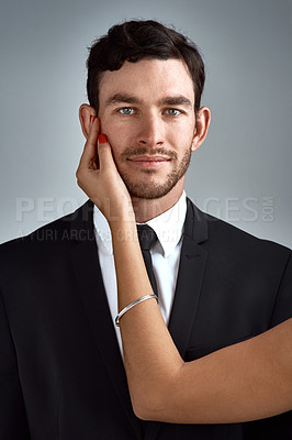 Buy stock photo Studio portrait of a handsome young businessman being touched by an unrecognizable woman’s hand against a gray background