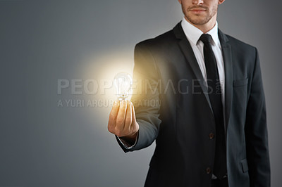 Buy stock photo Cropped studio shot of a businessman holding a glowing lightbulb against a gray background