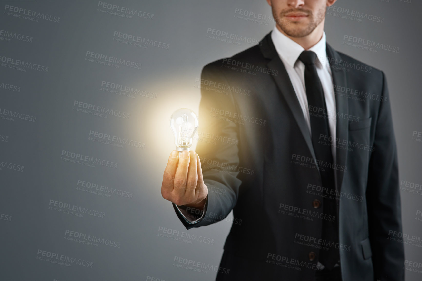 Buy stock photo Cropped studio shot of a businessman holding a glowing lightbulb against a gray background