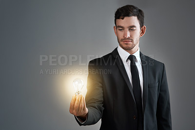 Buy stock photo Studio shot of a young businessman holding a glowing lightbulb against a gray background