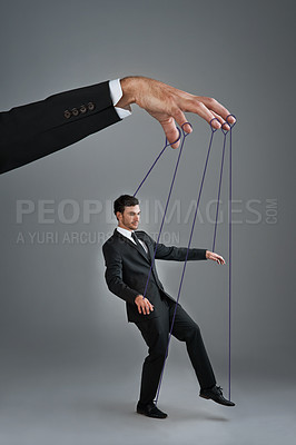 Buy stock photo Studio shot of a young businessman being controlled like a puppet by a giant hand against a gray background